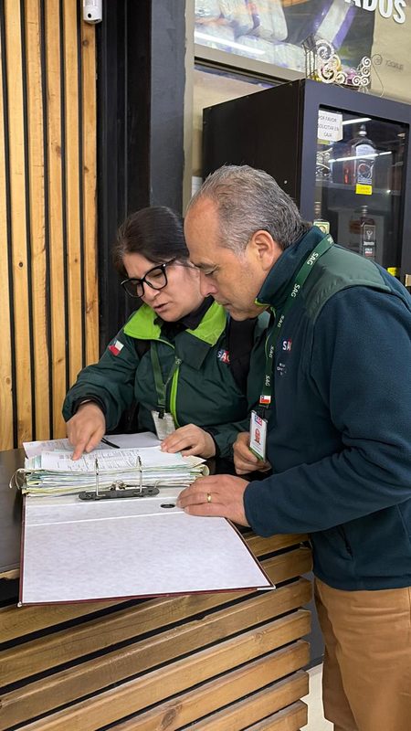Fiscalizadores del Servicio Agrícola y Ganadero revisando etiquetas de botellas de alcohol en un establecimiento comercial