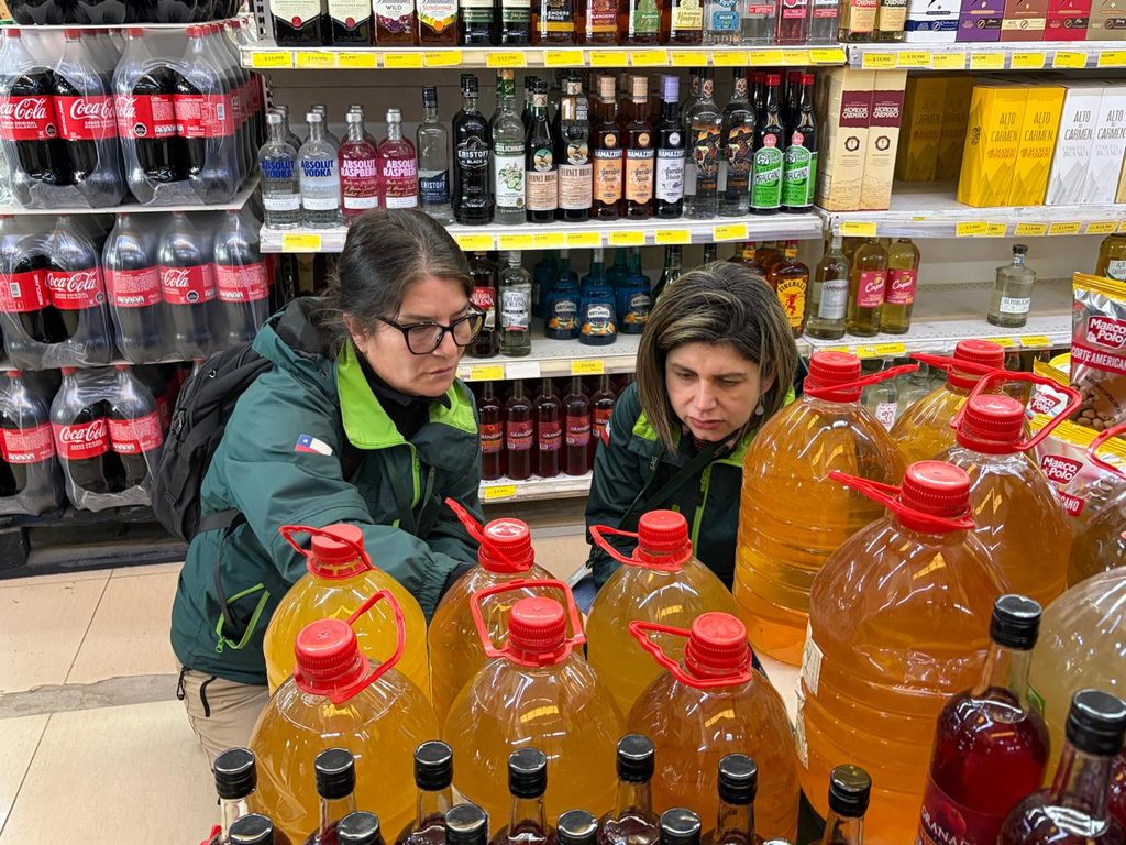 Fiscalizadores del Servicio Agrícola y Ganadero revisando etiquetas de botellas de alcohol en un establecimiento comercial