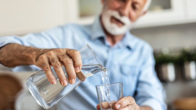 Persona mayor bebiendo agua para prevenir la deshidratación silenciosa en primavera.
